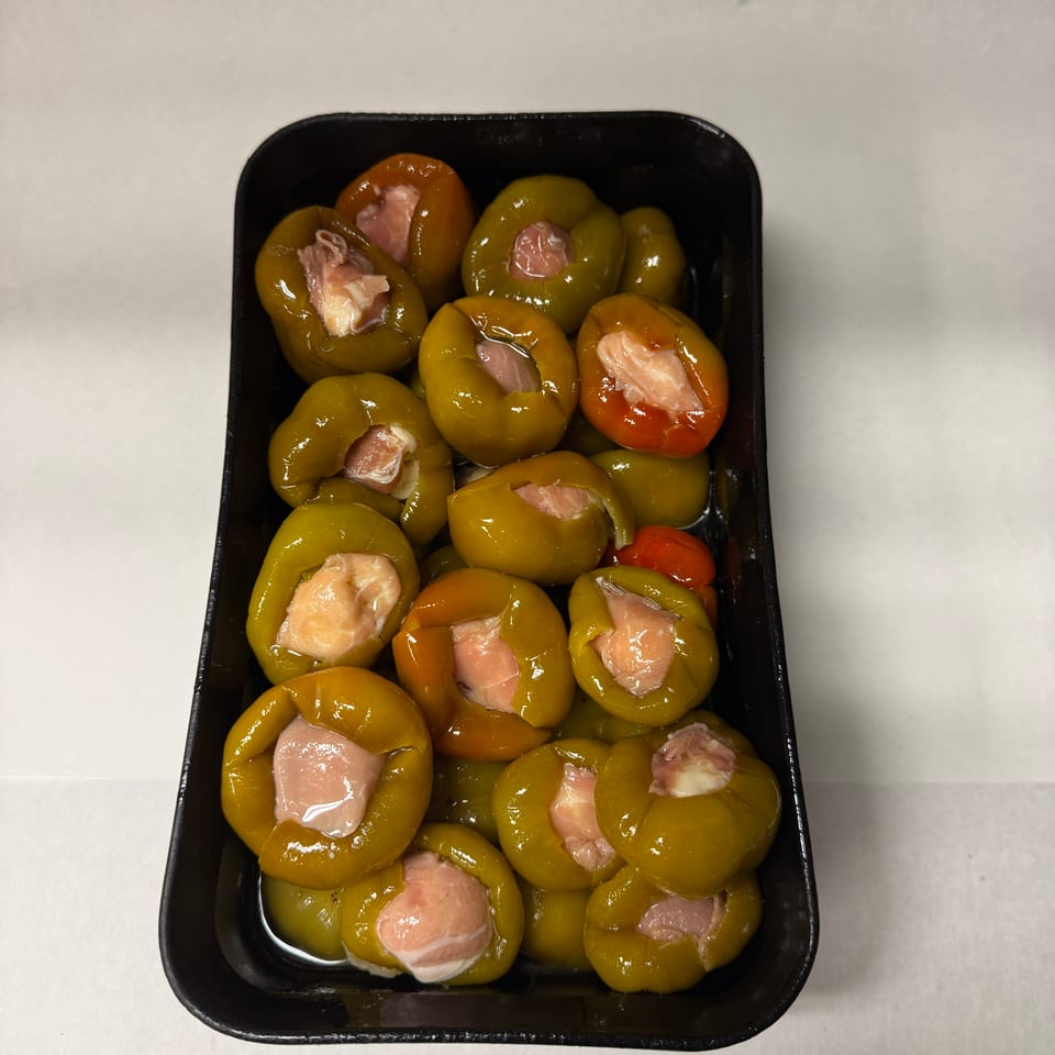 Black tray filled with glossy green and orange peppers stuffed with pieces of pink meat.