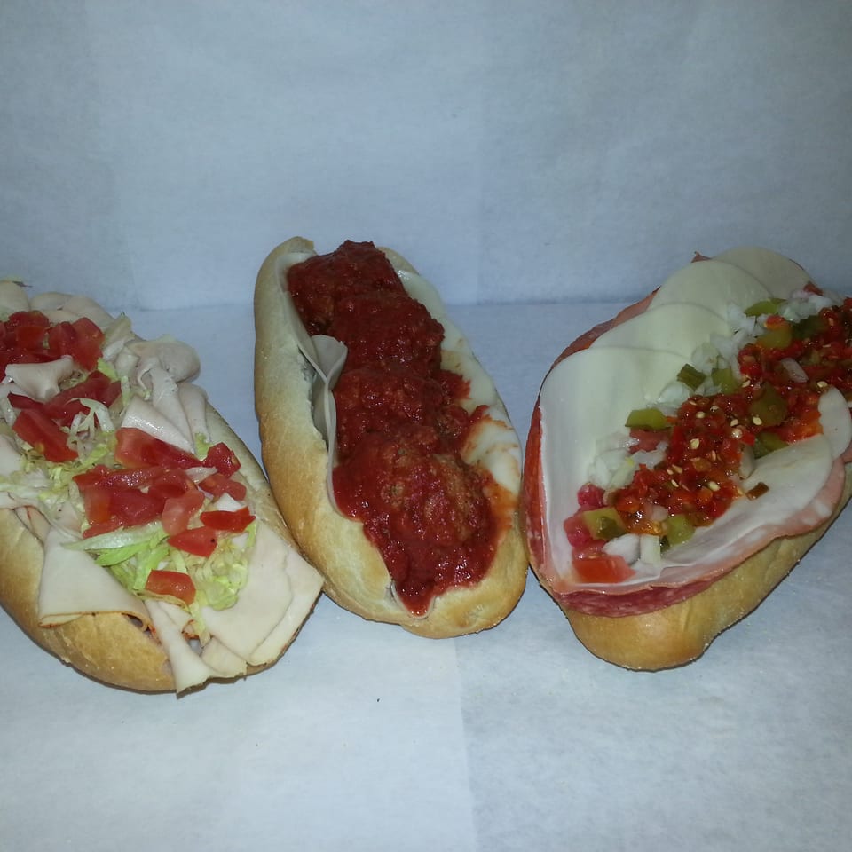 Three assorted submarine sandwiches with deli meats, meatballs, cheese, lettuce, tomatoes, onions, and peppers.