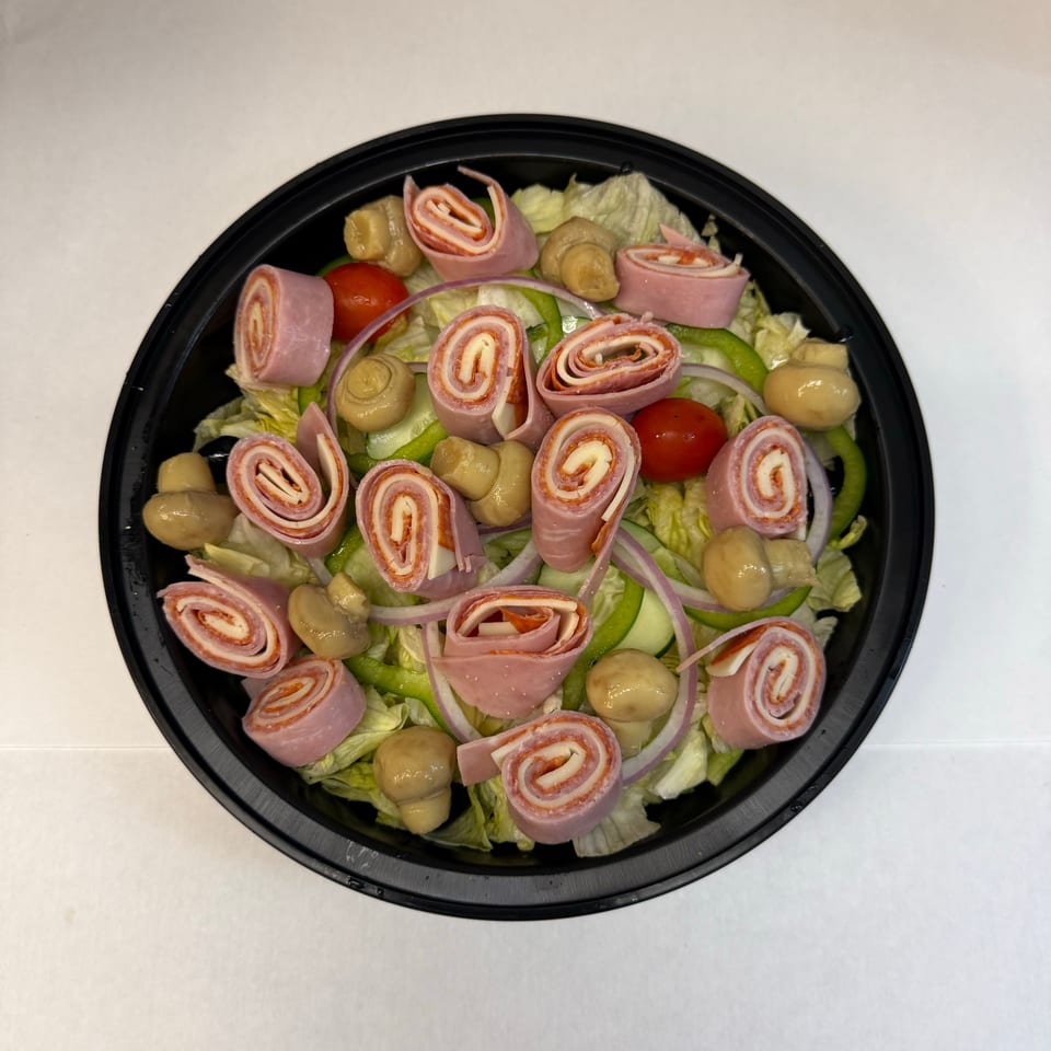 Black bowl of lettuce salad topped with rolled ham and cheese, mushrooms, tomatoes, cucumbers, green peppers, and red onion.
