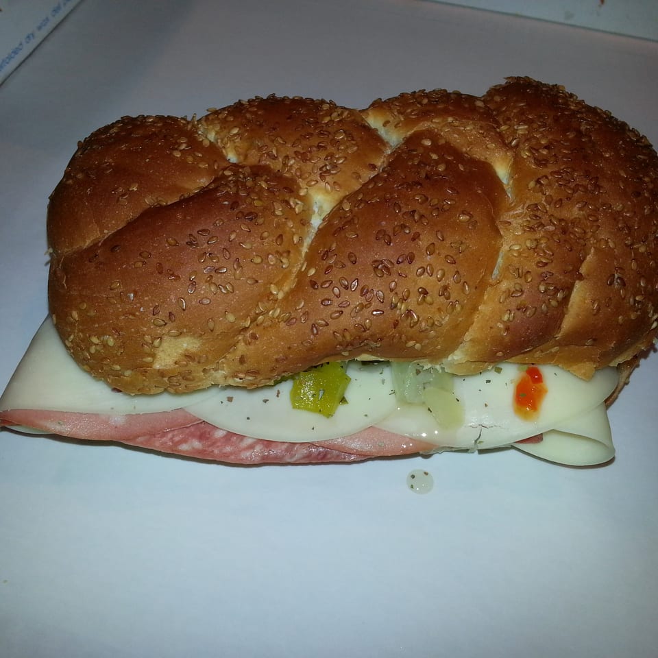 Sesame-topped braided sandwich filled with sliced ham, cheese, pickles, onions, herbs, and red sauce.